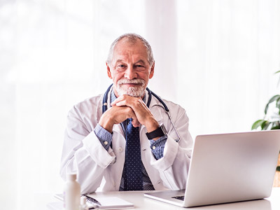Älterer Arzt sitzt am Schreibtisch in seiner Praxis